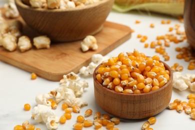 Photo of Corn kernels and tasty popcorn on white table, closeup