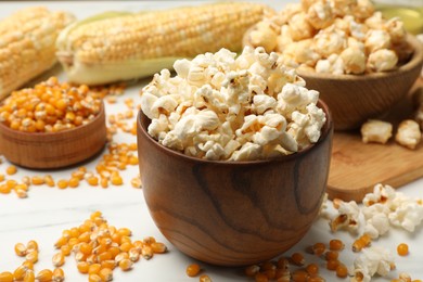 Photo of Tasty popcorn and corn kernels on white table, closeup