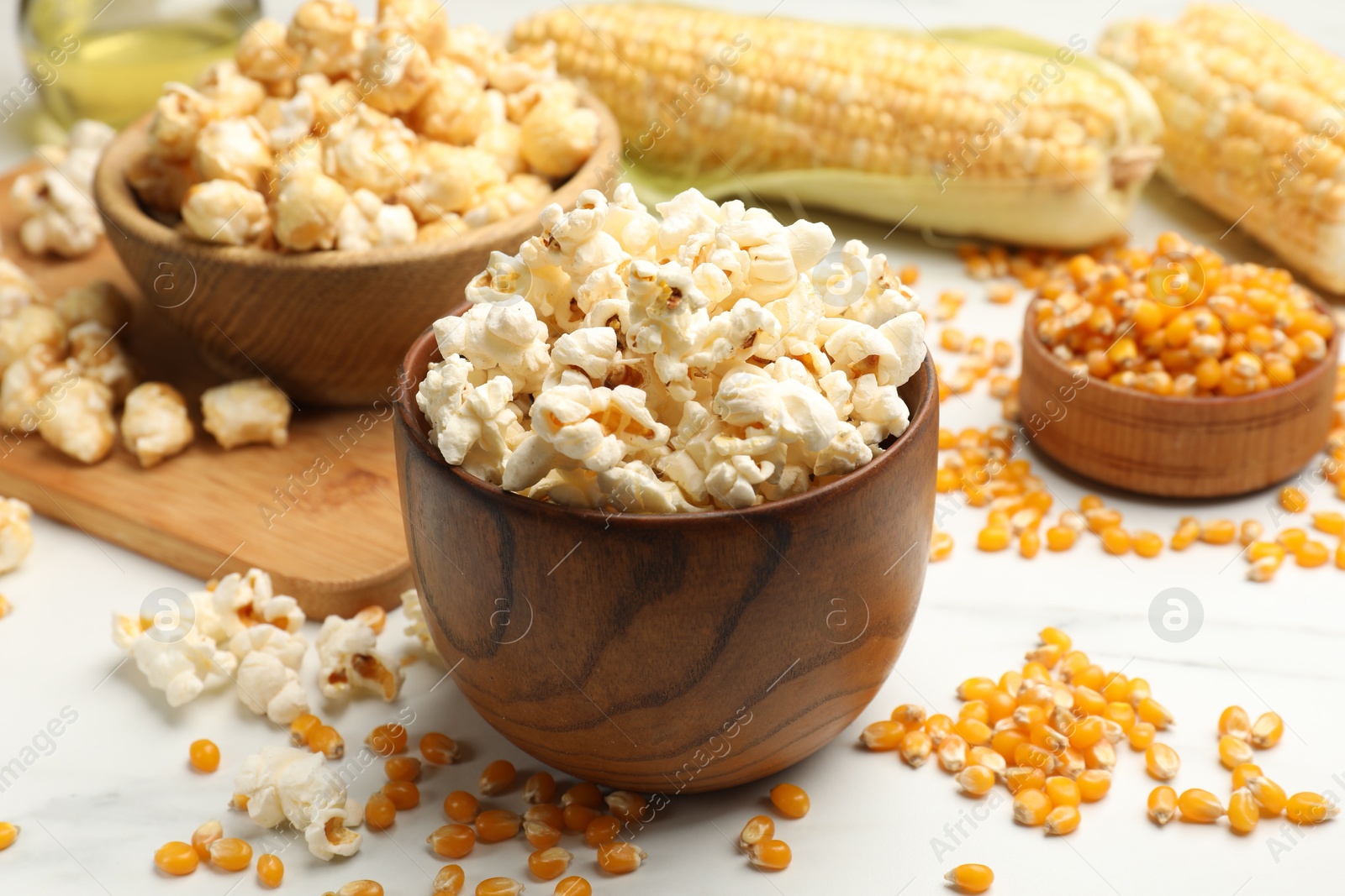 Photo of Tasty popcorn and corn kernels on white table, closeup