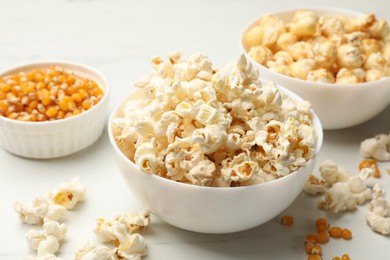 Photo of Tasty popcorn and corn kernels on white table, closeup