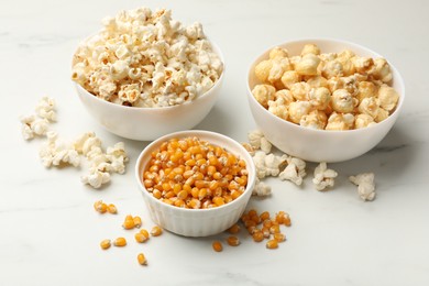 Photo of Tasty popcorn and corn kernels on white table, closeup