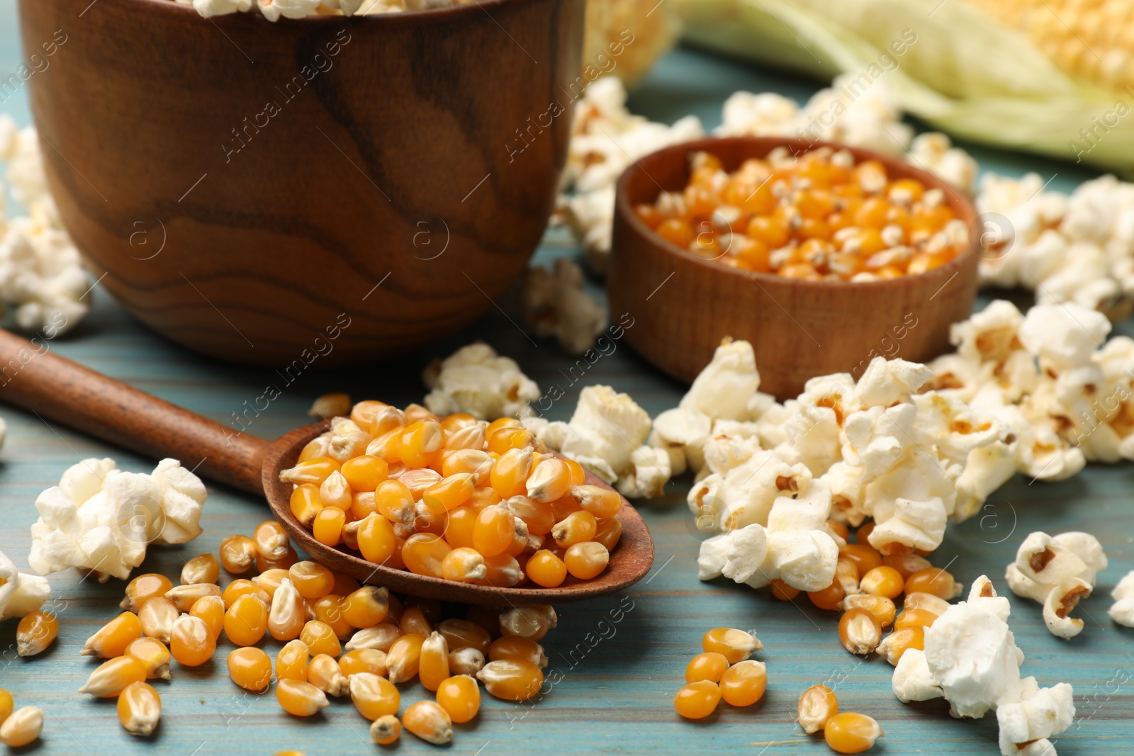 Photo of Corn kernels and tasty popcorn on blue wooden table, closeup