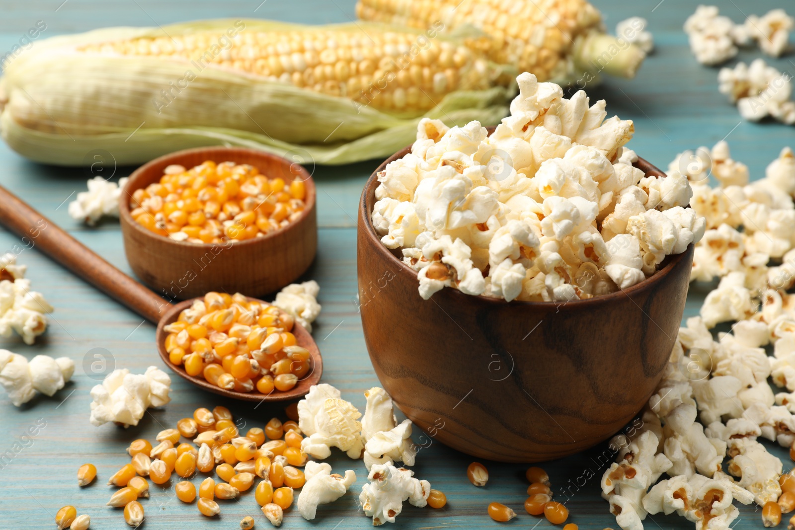 Photo of Tasty popcorn and corn kernels on blue wooden table, closeup