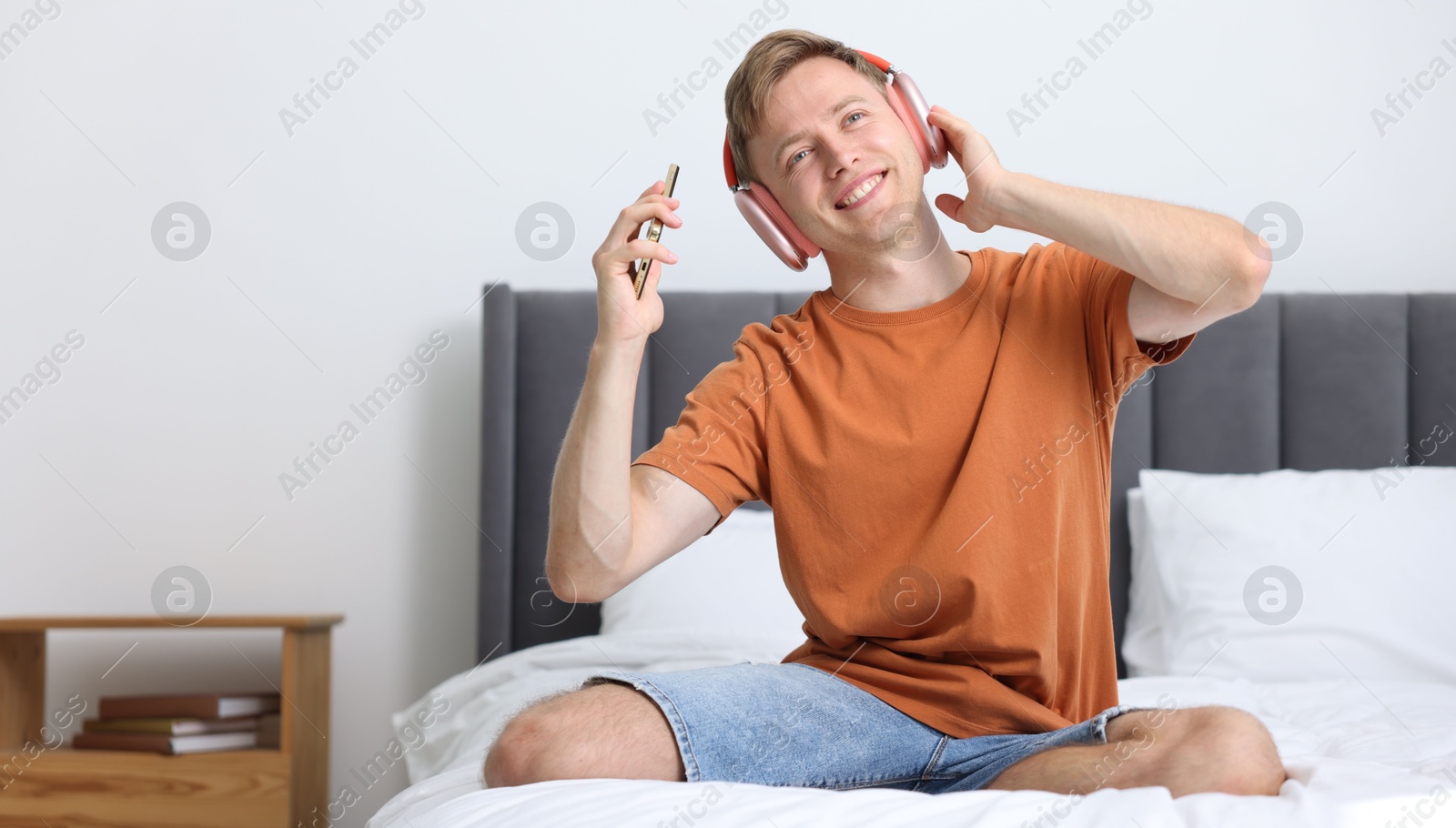 Photo of Happy man with smartphone listening to music in headphones on bed at home