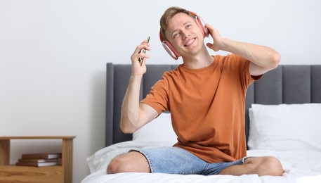 Photo of Happy man with smartphone listening to music in headphones on bed at home