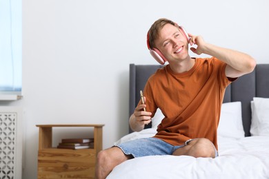Photo of Happy man with smartphone listening to music in headphones on bed at home. Space for text
