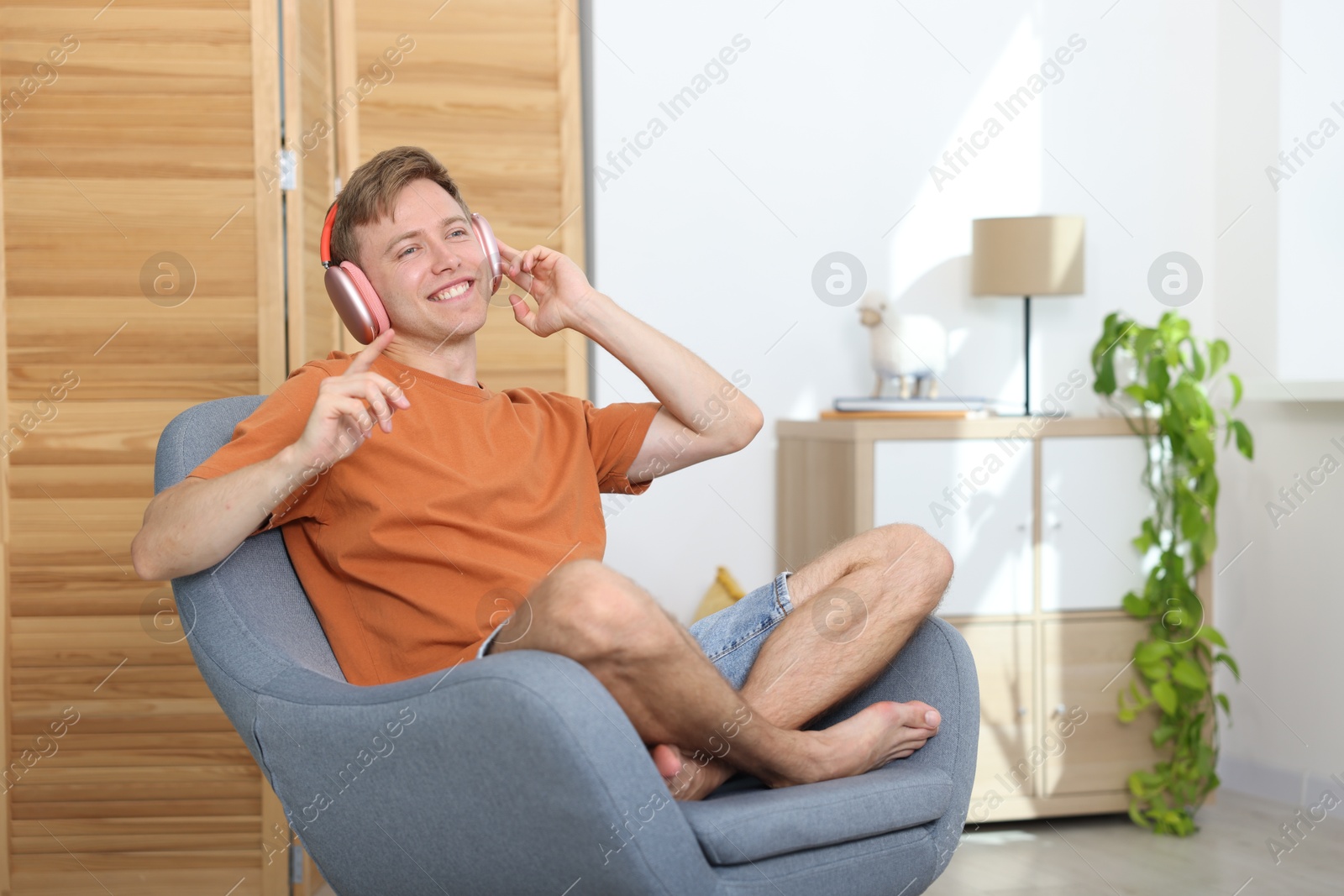 Happy man with headphones listening to music in armchair at home. Space for text Photo of Happy man with headphones listening to music in armchair at home. Space for text