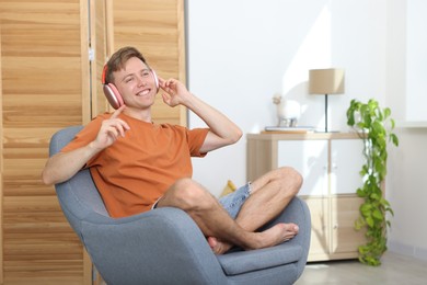 Photo of Happy man with headphones listening to music in armchair at home. Space for text