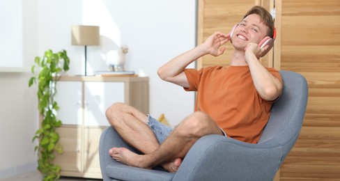 Photo of Happy man with headphones listening to music in armchair at home. Space for text