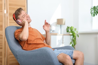 Photo of Happy man with headphones listening to music in armchair at home. Space for text