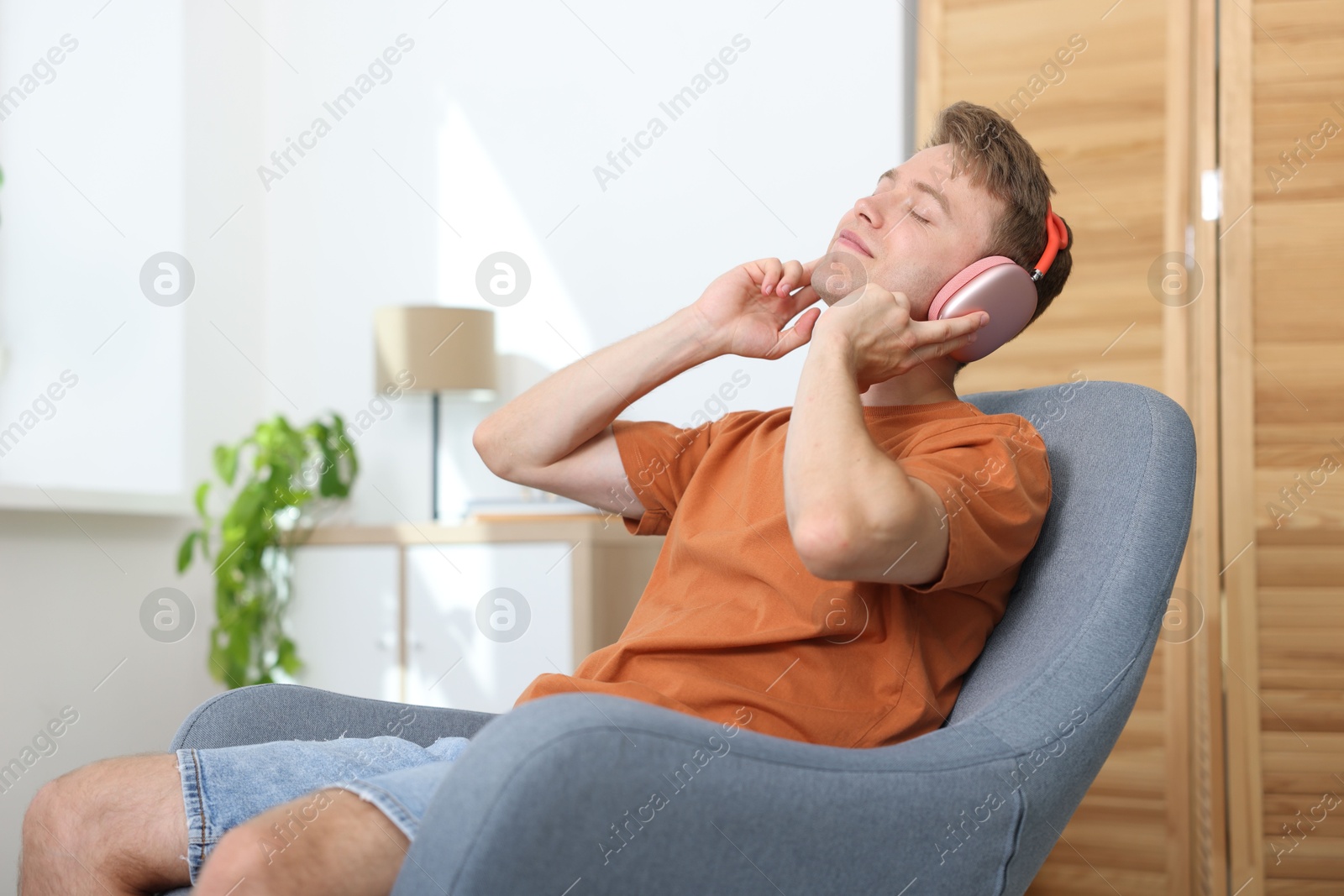 Happy man with headphones listening to music in armchair at home Photo of Happy man with headphones listening to music in armchair at home