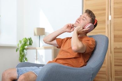 Photo of Happy man with headphones listening to music in armchair at home