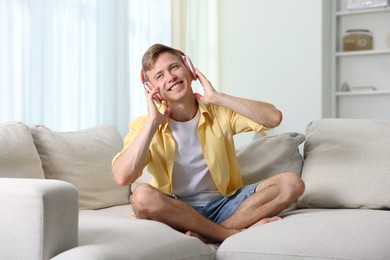 Photo of Happy man listening to music in headphones on sofa at home