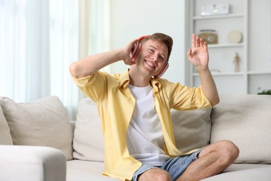Photo of Happy man listening to music in headphones on sofa at home