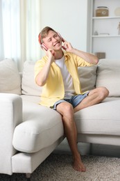 Photo of Happy man listening to music in headphones on sofa at home