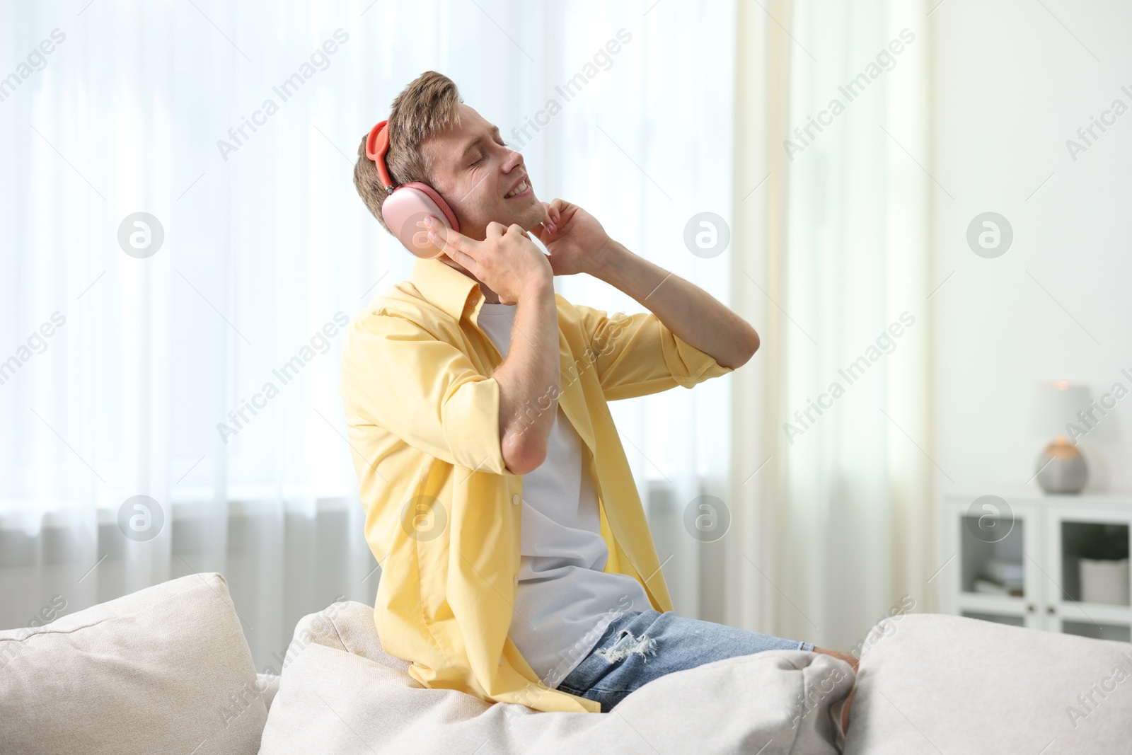 Happy man listening to music in headphones on sofa at home Photo of Happy man listening to music in headphones on sofa at home