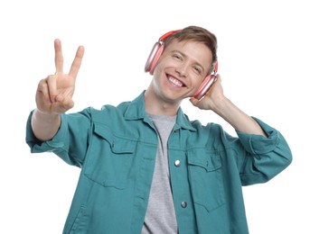 Photo of Happy man listening to music in headphones and showing peace sign on white background