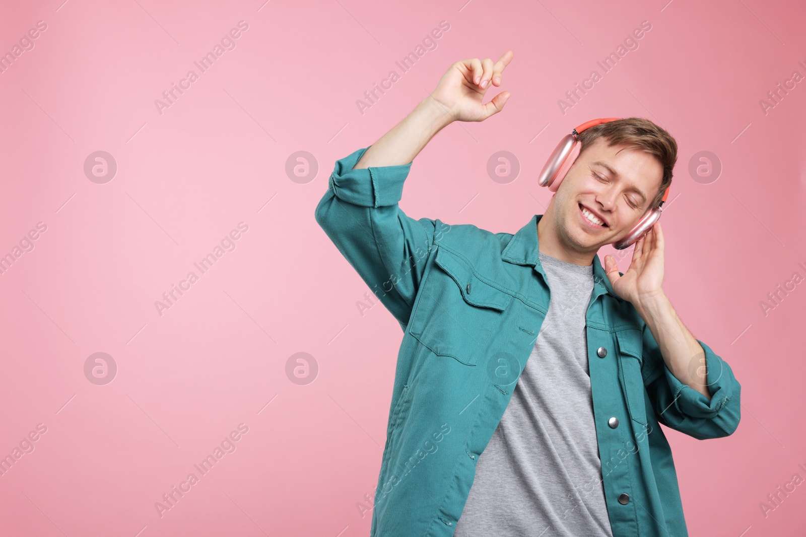 Happy man listening to music in headphones and dancing on pink background. Space for text Photo of Happy man listening to music in headphones and dancing on pink background. Space for text