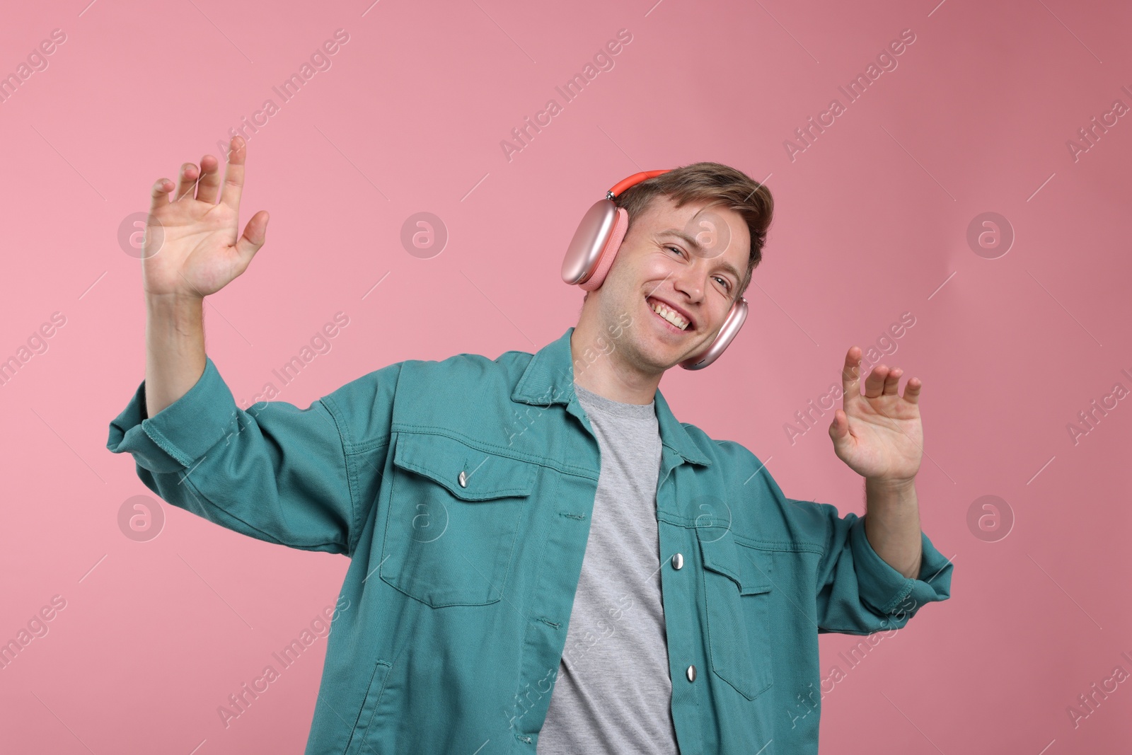 Happy man listening to music in headphones and dancing on pink background Photo of Happy man listening to music in headphones and dancing on pink background