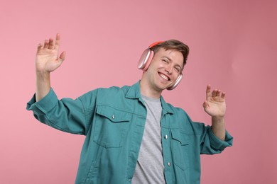 Photo of Happy man listening to music in headphones and dancing on pink background