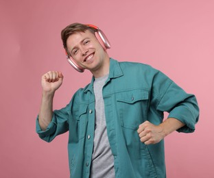 Photo of Happy man listening to music in headphones and dancing on pink background