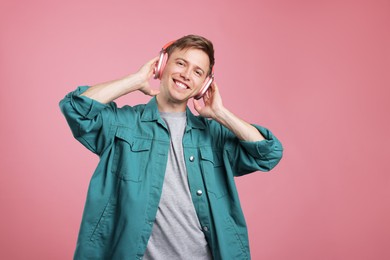Photo of Happy man listening to music in headphones and dancing on pink background