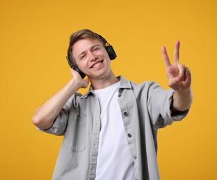 Photo of Happy man listening to music in headphones and showing peace sign on yellow background