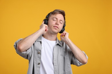 Photo of Young man listening to music in headphones and dancing on yellow background