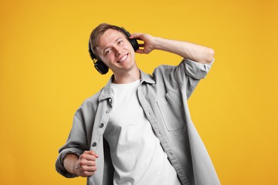 Photo of Happy man listening to music in headphones and dancing on yellow background