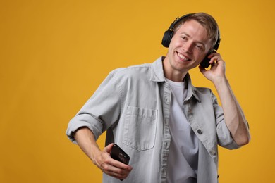 Photo of Happy man with smartphone listening to music in headphones on yellow background. Space for text