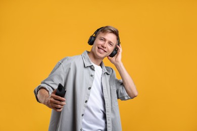 Photo of Happy man with smartphone listening to music in headphones on yellow background
