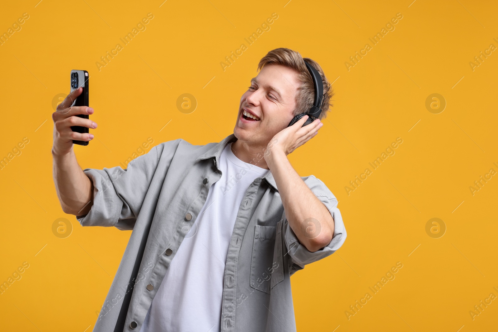 Happy man with smartphone listening to music in headphones on yellow background Photo of Happy man with smartphone listening to music in headphones on yellow background