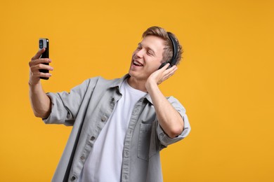 Photo of Happy man with smartphone listening to music in headphones on yellow background