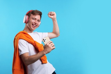 Photo of Happy man with smartphone listening to music in headphones on light blue background. Space for text