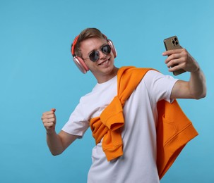 Photo of Happy man with smartphone listening to music in headphones on light blue background