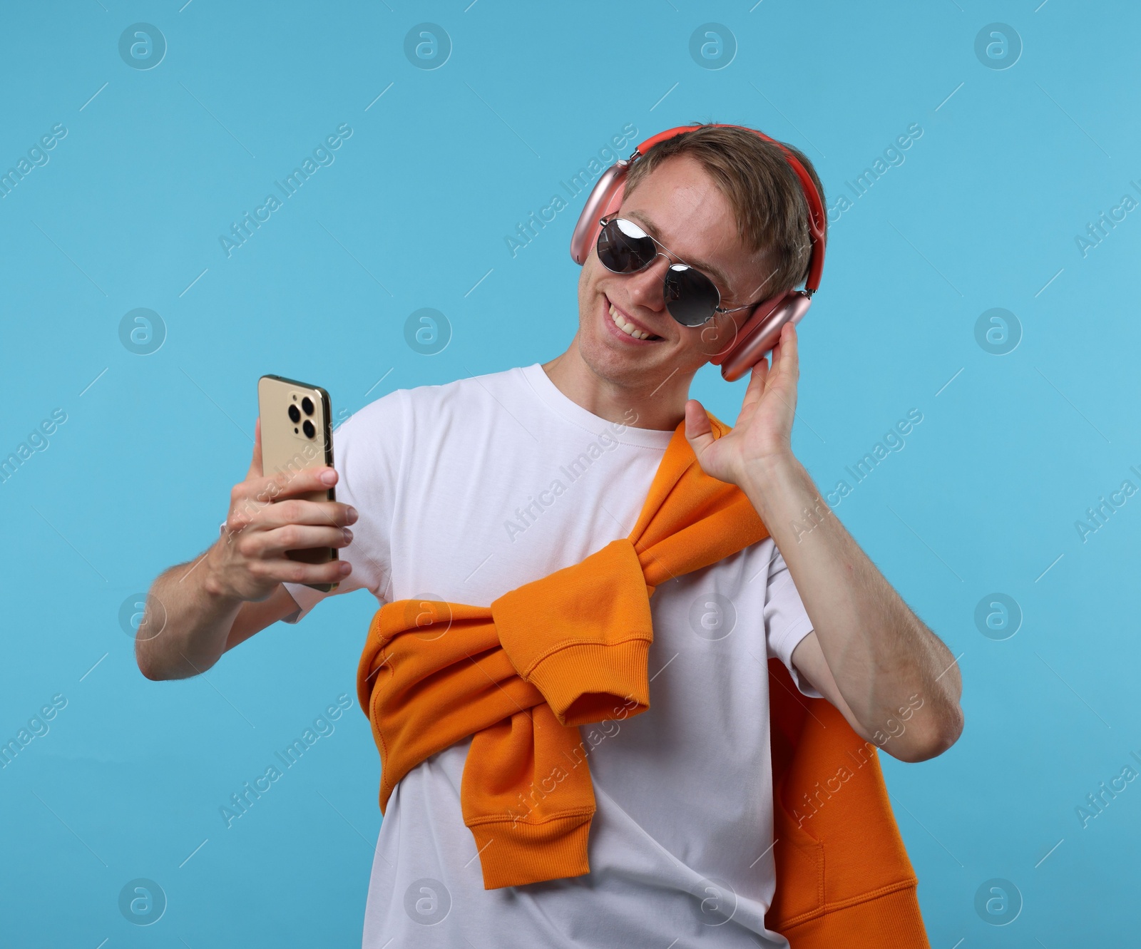 Happy man with smartphone listening to music in headphones on light blue background Photo of Happy man with smartphone listening to music in headphones on light blue background