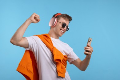 Photo of Happy man with smartphone listening to music in headphones on light blue background
