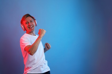 Photo of Happy man listening to music in headphones on blue background with neon light. Space for text