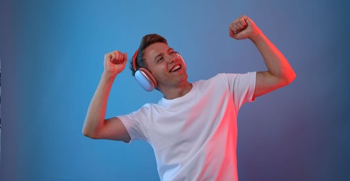 Photo of Happy man listening to music in headphones on blue background with neon light