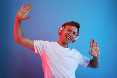 Photo of Happy man listening to music in headphones on blue background with neon light