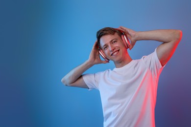 Photo of Happy man listening to music in headphones on blue background with neon light. Space for text