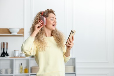 Photo of Happy woman with smartphone listening to music in headphones at home