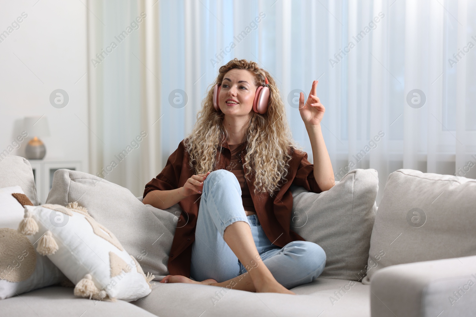 Photo of Happy woman listening to music in headphones on sofa at home