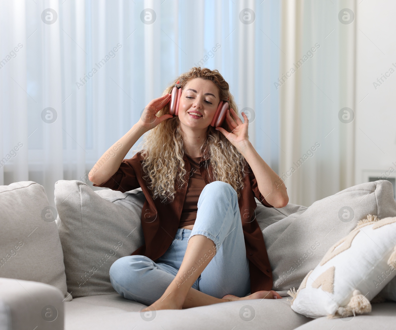 Happy woman listening to music in headphones on sofa at home Photo of Happy woman listening to music in headphones on sofa at home