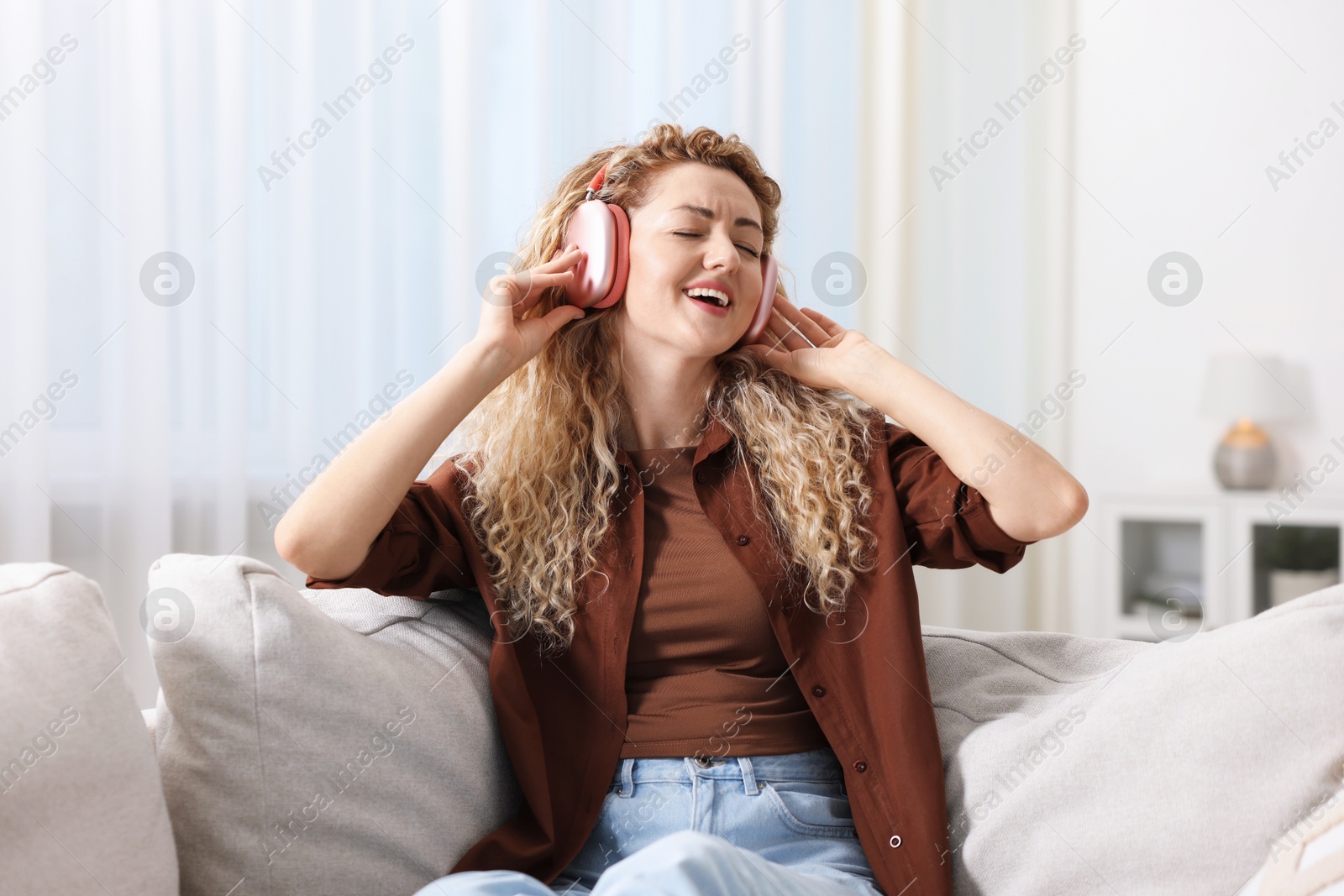 Happy woman listening to music in headphones on sofa at home Photo of Happy woman listening to music in headphones on sofa at home