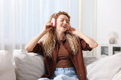 Photo of Happy woman listening to music in headphones on sofa at home