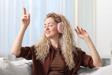 Photo of Happy woman listening to music in headphones on sofa at home