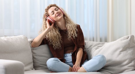 Photo of Happy woman listening to music in headphones on sofa at home