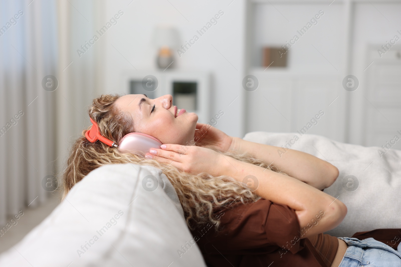 Happy woman listening to music in headphones on sofa at home Photo of Happy woman listening to music in headphones on sofa at home