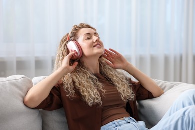 Photo of Happy woman listening to music in headphones on sofa at home